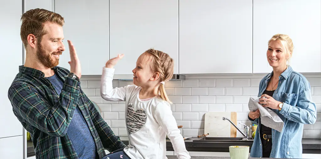 Junge Familie in moderner weißer Küche mit Eltern und Kind beim gemeinsamen Spielen und Kochen, hochwertige Einbauküche mit klaren Fronten, Wohnküche als Mittelpunkt für Alltag, Familie und gemeinsames Leben.